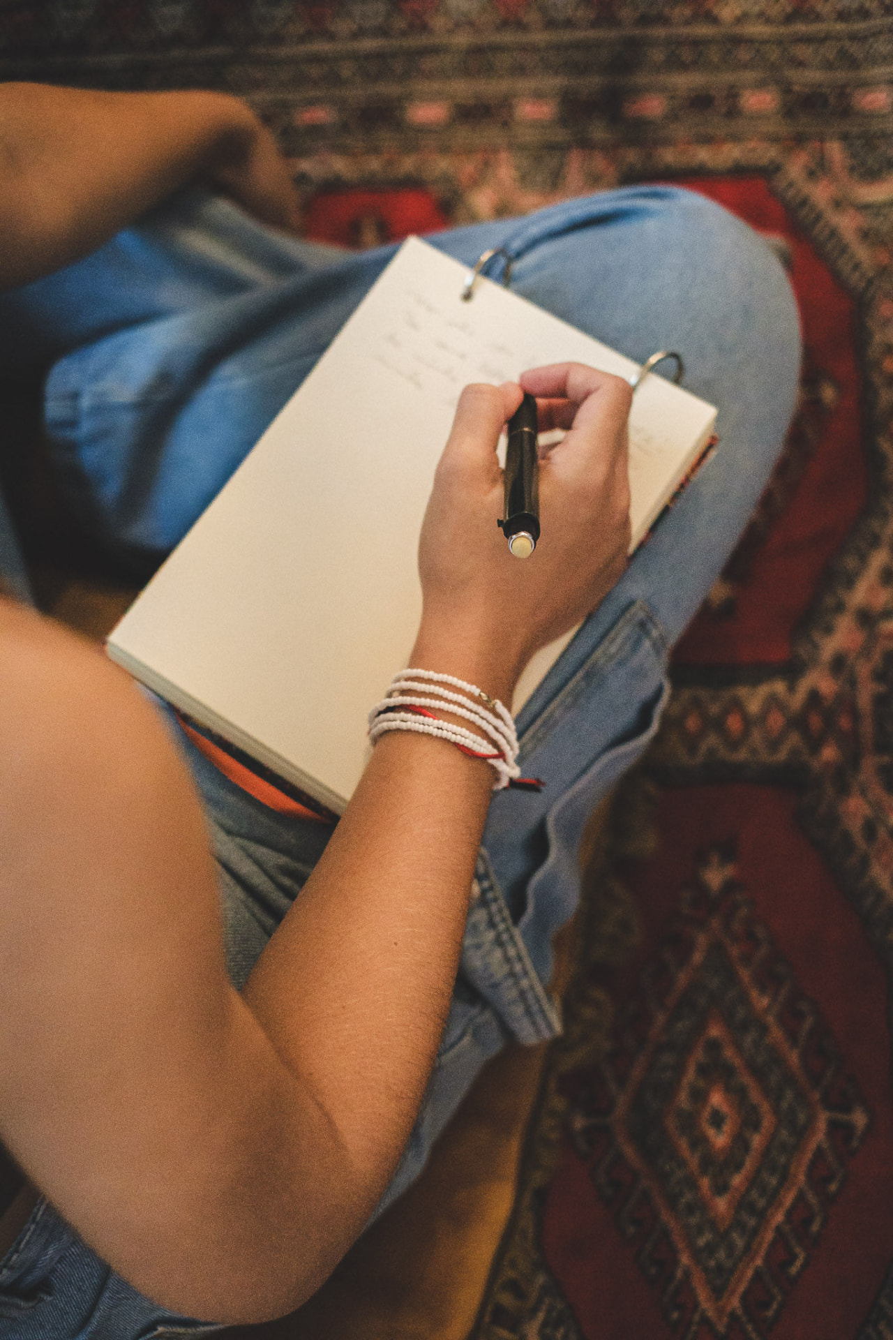 Mulher sentada no tapete escrevendo em um caderno apoiado no colo